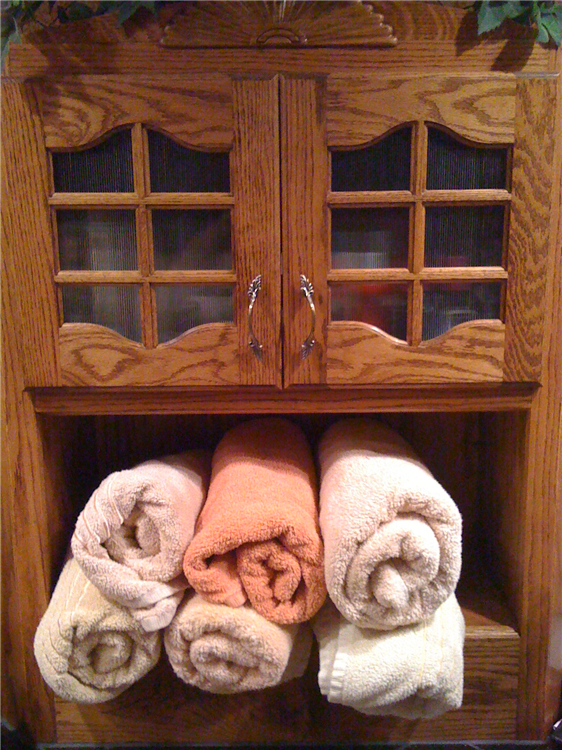 A Custom Stained Red Oak Linen Cabinet With Glass Inserts and Bath Towel Rolls